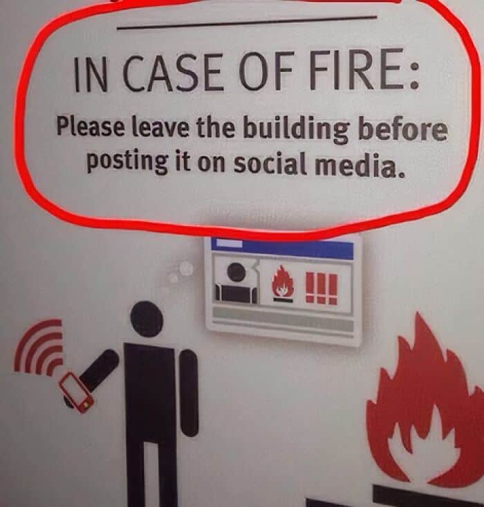 Fire warning sign humorously advising evacuation before social media posts. Fire warning sign humorously advising evacuation before social media posts.